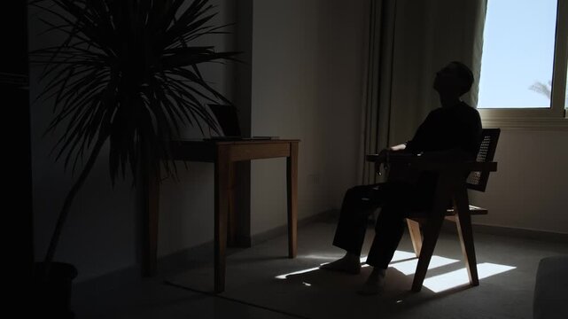 Silhouette of a thoughtful man sitting alone in a dark room and looking up at the ceiling, lost in deep thought, overthinking and uncertainty, reflecting inner struggle and mental fatigue