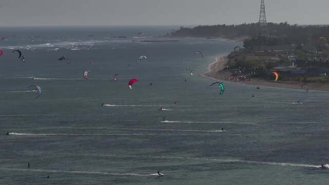 Aerial drone view of kite surfers riding the waves at My Hoa Beach in Vinh Hai, Khanh Hoa, Vietnam, showcasing a spectacular coastal landscape under bright sunlight.
