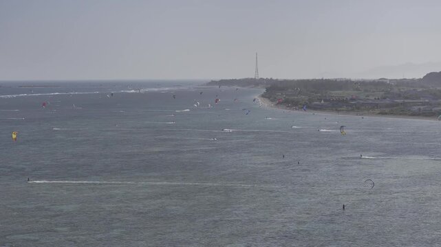 Aerial drone view of kite surfers riding the waves at My Hoa Beach in Vinh Hai, Khanh Hoa, Vietnam, showcasing a spectacular coastal landscape under bright sunlight.
