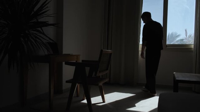 Silhouette of stressed man pacing back and forth near a window, talking to himself and gesturing with his hands, overwhelmed by thoughts, mental pressure, frustration and inner conflict
