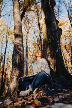 Vertical portrait of a peaceful mid-adult woman sitting in a lotus position by a tree trunk in autumn forest.