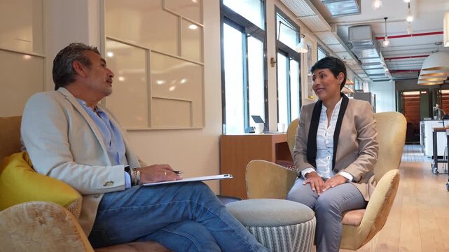 Middle aged coworkers having an informal business meeting in a contemporary office lounge. The man is holding a clipboard and talking