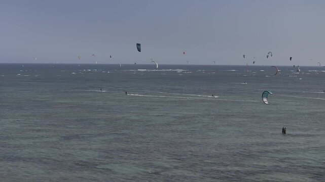 Aerial drone view of kite surfers riding the waves at My Hoa Beach in Vinh Hai, Khanh Hoa, Vietnam, showcasing a spectacular coastal landscape under bright sunlight. 