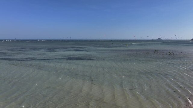 Aerial drone view of kite surfers riding the waves at My Hoa Beach in Vinh Hai, Khanh Hoa, Vietnam, showcasing a spectacular coastal landscape under bright sunlight. 