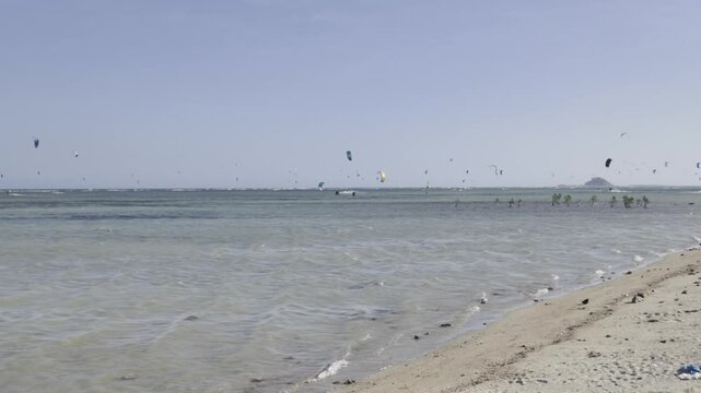 Aerial drone view of kite surfers riding the waves at My Hoa Beach in Vinh Hai, Khanh Hoa, Vietnam, showcasing a spectacular coastal landscape under bright sunlight. 
