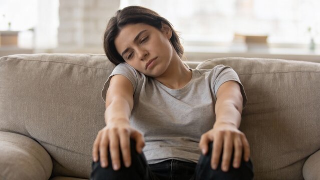 exhausted young caucasian woman, resting head on sofa arm, wearing grey t shirt, feeling tired, depressed, lonely, indoor home setting