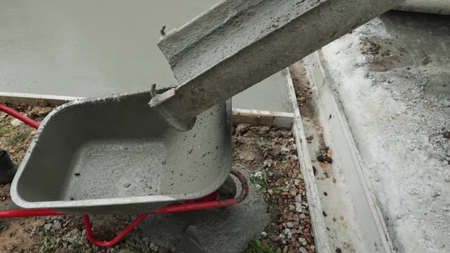 Wet concrete flows from a mixer chute into a wheelbarrow at a construction site, concrete delivery and building process.