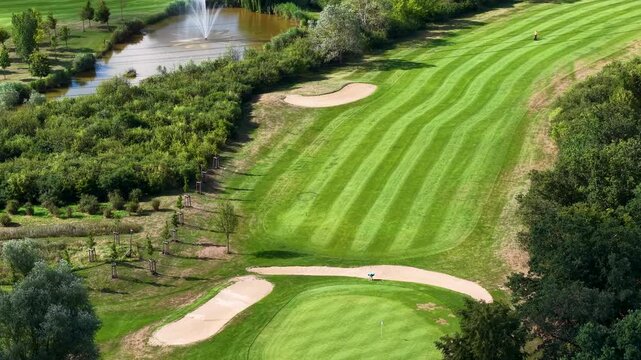 Aerial view of Magdeburg golf course shows striped fairways, golfcar, sand bunkers, pond fountain dense woodland. Summer landscape combines sport, water, manicured lawns and lush greenery
