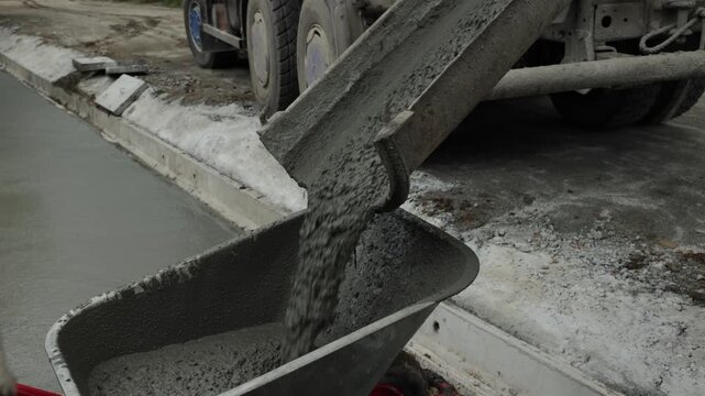 Wet concrete pours from a mixer chute into a wheelbarrow at a construction site, concrete delivery and building process.