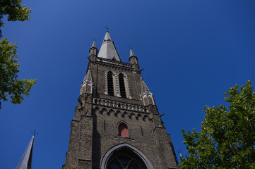 Fototapeta premium Imposing gothic brick church tower with arched windows and pointed spires against a clear blue sky. Historic medieval European religious architecture.
