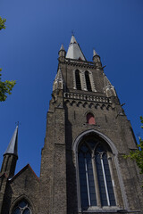 Fototapeta premium Imposing gothic brick church tower with arched windows and pointed spires against a clear blue sky. Historic medieval European religious architecture.