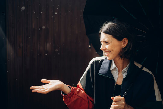 Smiling woman holds umbrella and catches rain outdoors