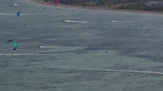 Aerial drone view of kite surfers riding the waves at My Hoa Beach in Vinh Hai, Khanh Hoa, Vietnam, showcasing a spectacular coastal landscape under bright sunlight. 