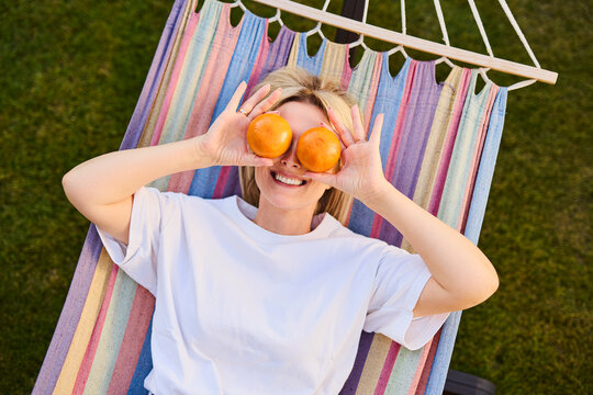 Woman lying in hammock holding oranges over eyes in backyard summer fun