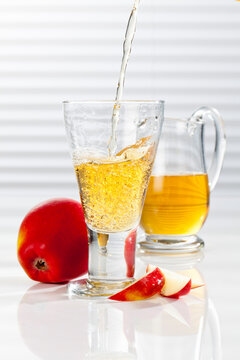 Carafe and glass with pouring apple juice, close up