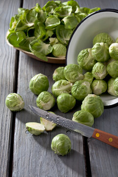 Bowl of Brussels sprouts, plate with peels and kitchen knife on grey wooden table