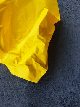 Crumpled yellow paper lies on a dark textured concrete surface