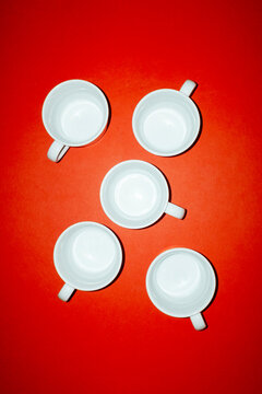 Five empty white coffee cups sit on a bright red background