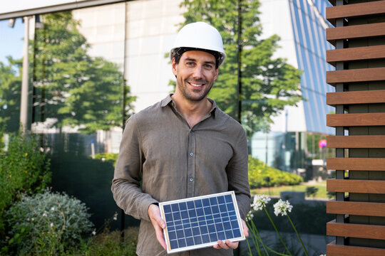 Smiling photovoltaic technician holds a solar panel outdoors