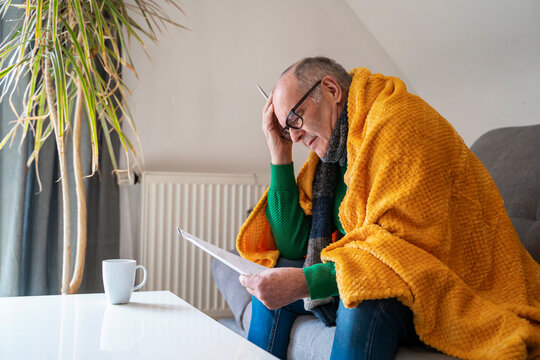 Man under blanket checking heating costs and finances indoors
