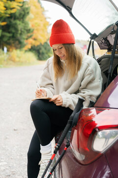 Smiling woman writes a journal in a car trunk before a fall hike