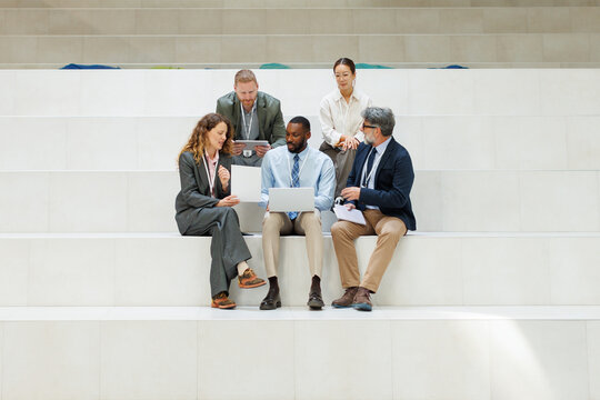 A diverse business team discusses strategy on white office steps