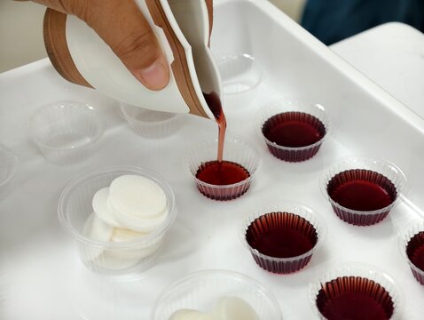 Close-up of preparing Holy Communion elements, pouring grape juice into cups alongside Communion wafers. Perfect for Christian church services, Easter, and religious concepts.