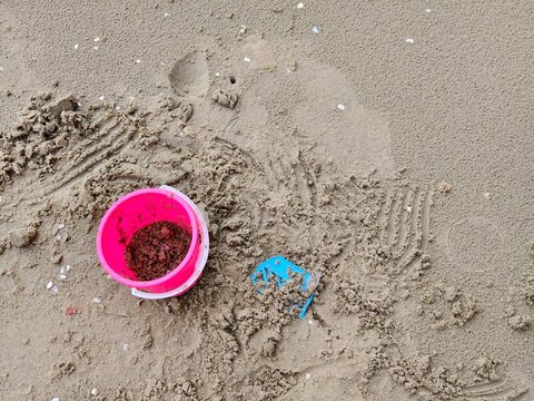 A top-down view of a child's pink beach bucket filled with sand and a blue mold on the wet, disturbed sand. Perfect for summer, vacation, family travel, and parenting concepts.