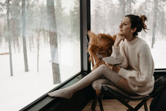 Woman enjoys the snowy forest view from a cozy winter cabin