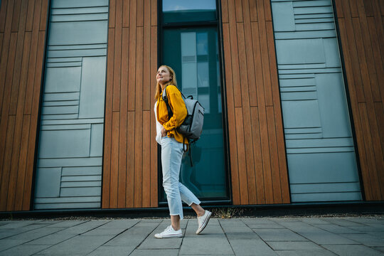 A confident businesswoman carries a backpack near a modern building