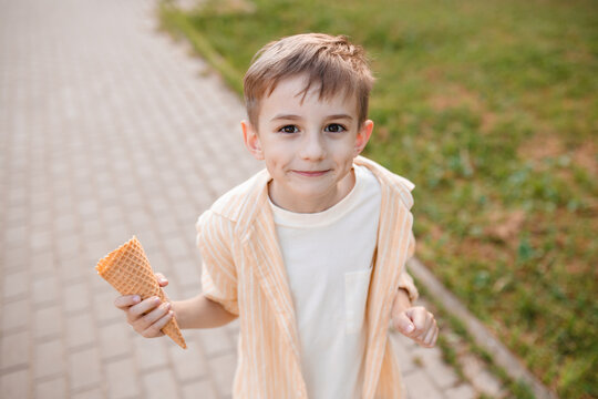 A smiling boy holds an ice cream cone outdoors on a summer day