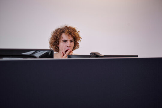 Young man in office yawning behind computer screen
