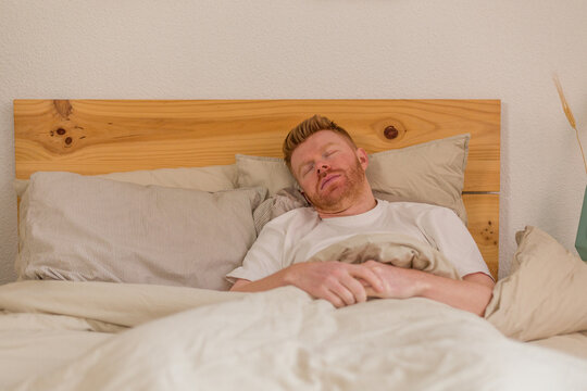 Man with ginger hair sleeping peacefully in bed in the morning