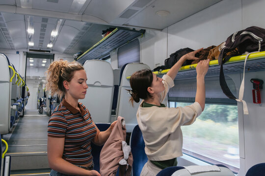 Woman puts luggage on the overhead rack inside a train