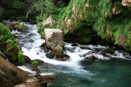 Beautiful turquoise water basin at the natural source of Krka river under a rocky cliff. Crystal clear stream in wild nature environment, Croatia.