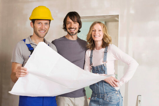 Young couple and construction worker holding construction plan, smiling, portrait