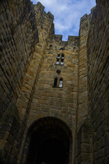 Majestic medieval stone castle fortress featuring ancient defense walls, battlements, and tall towers surrounded by green grass under a cloudy sky. Alnwick castle England, towers a very old castle © TomKorcak