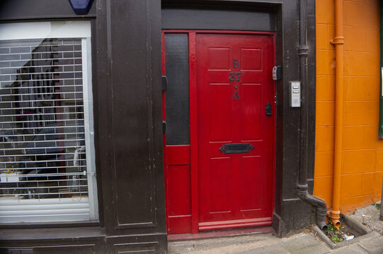 Bright red front door of urban residential apartment next to a closed storefront with metal security shutters. Mixed-use city architecture.
