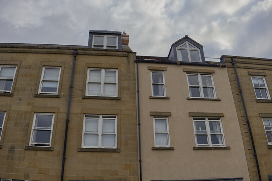 Exterior facade of adjacent residential buildings showing stone and rendered walls with windows and roof dormers against cloudy sky.