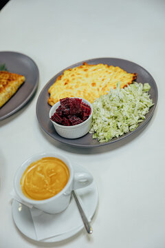 Baked golden savory dish served with shredded cabbage salad and beetroot in a ramekin, accompanied by a cup of coffee on a white table with copy space