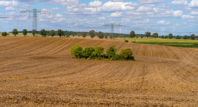 Weite Agrarlandschaft mit frisch gepfl&uuml;gtem Acker und Hochspannungsleitungen sowie Windkraftanlagen am Horizont, Uckermark, Brandenburg, Deutschland