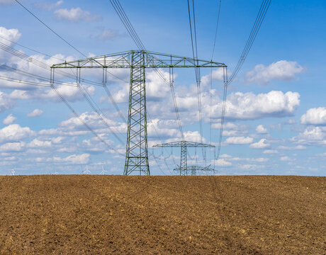 Weite Agrarlandschaft mit frisch gepfl&uuml;gtem Acker und Hochspannungsleitungen sowie Windkraftanlagen am Horizont, Uckermark, Brandenburg, Deutschland