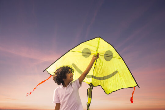Happy little boy holding a kite and trying to fly