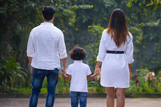 Back view of Indian parents with their son holding hands and walking in park