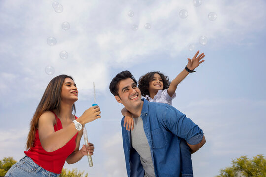 Happy parent with their son having fun with flying bubbles in the park