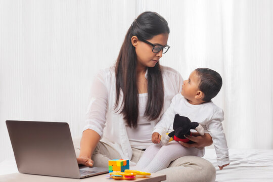 Mother holding child in her lap while using laptop