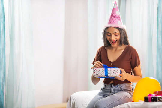 Excited young woman opening birthday gift while sitting on bed