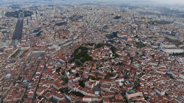 Stunning drone shot captures Lisbon at sunrise with Castelo Sao Jorge at the center and Liberdade Avenue in the distance, showcasing vibrant cityscape, golden light, and historic architecture.
