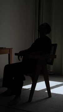 Emotionally exhausted man silhouette sitting alone in chair feeling defeated and overwhelmed during difficult period of life at home, vertical video