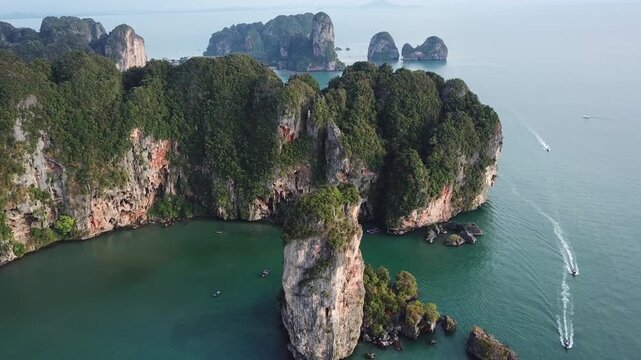 Aerial view of Railay Beach with dramatic limestone cliffs rising from turquoise water and long-tail boats leaving wakes in Ao Nang, Krabi, Thailand.